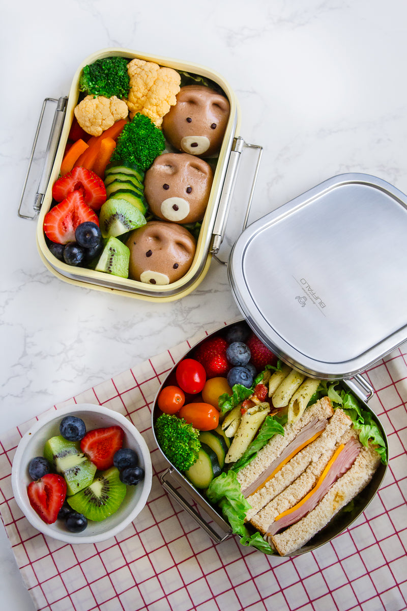 Healthy lunchboxes with sandwiches, fruits, and vegetables on a marbled background.