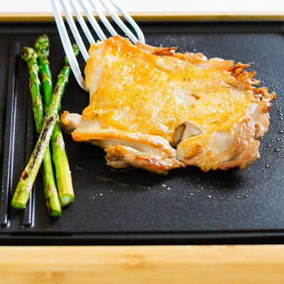 Grilled chicken thigh and asparagus on a black grill pan.