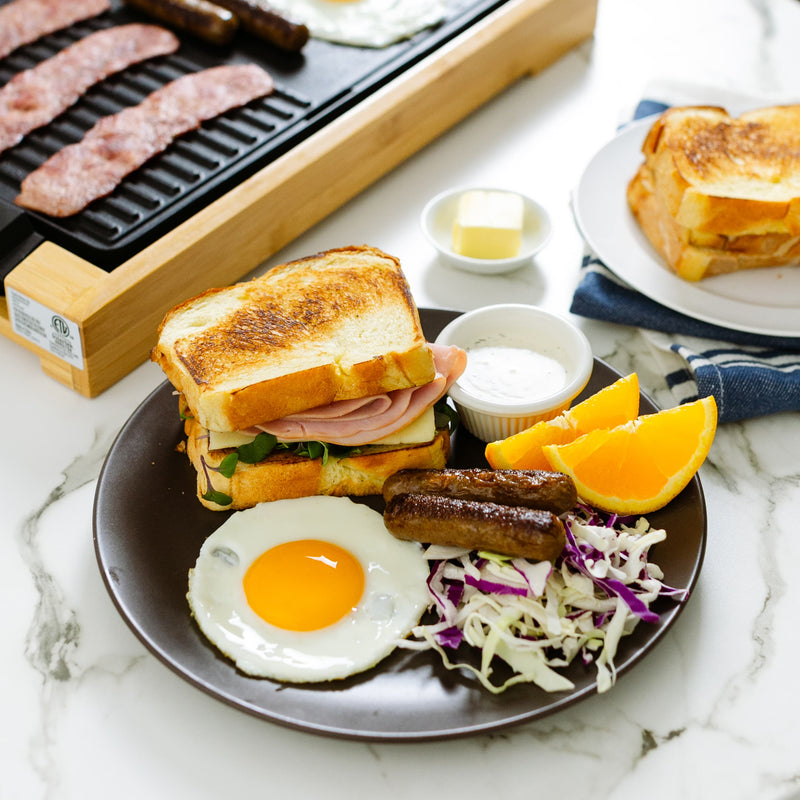 A breakfast plate with a sandwich, sausages, fried egg, coleslaw, and orange slices.